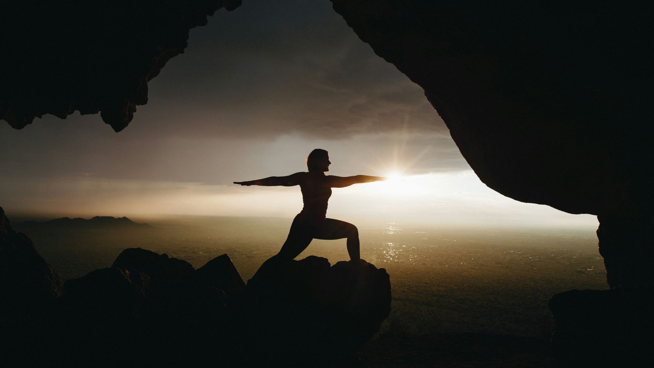 Man doing warrior yoga pose under rocks at the ocean